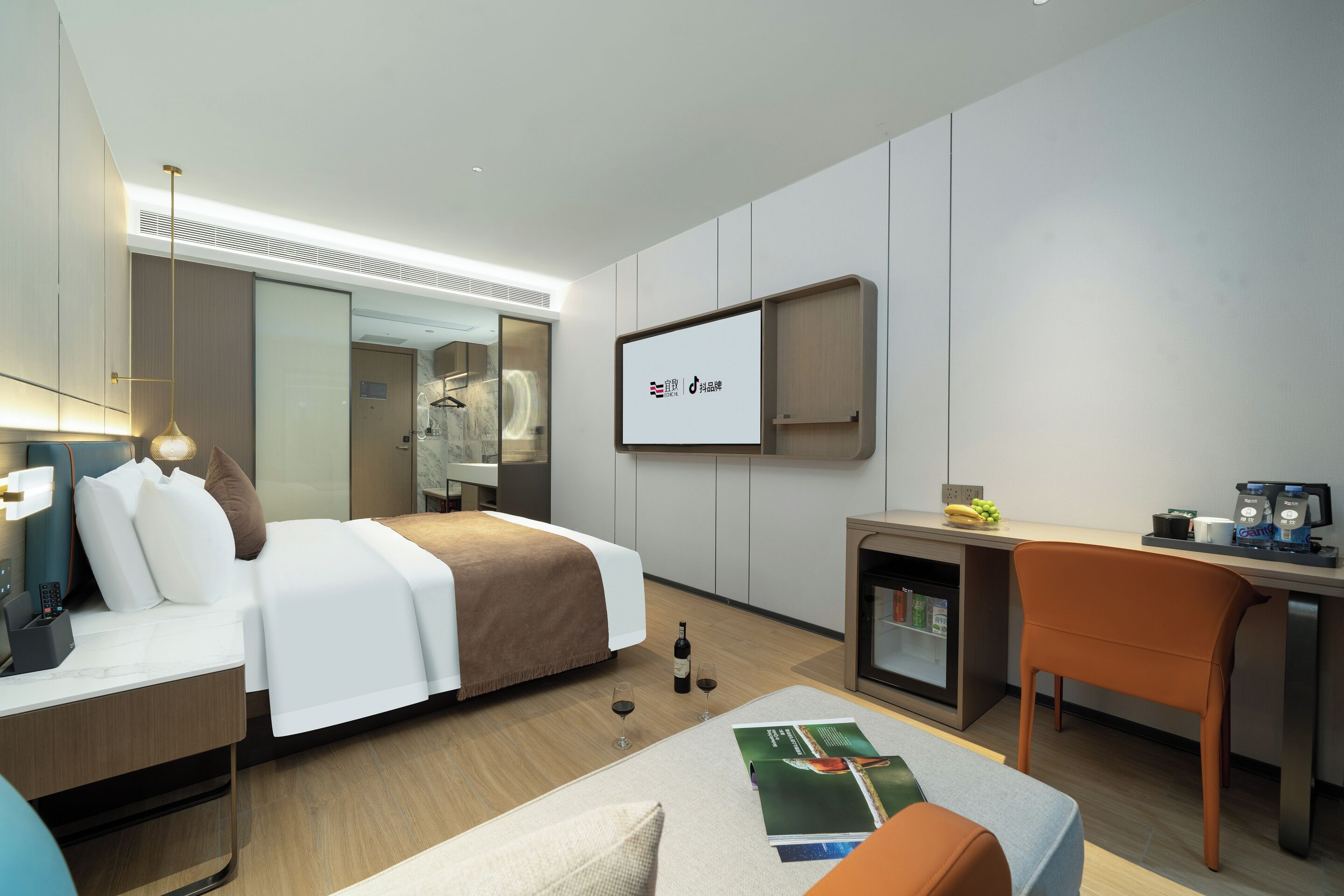 A modern hotel room with a bed, desk, chair, and a television displaying a logo.