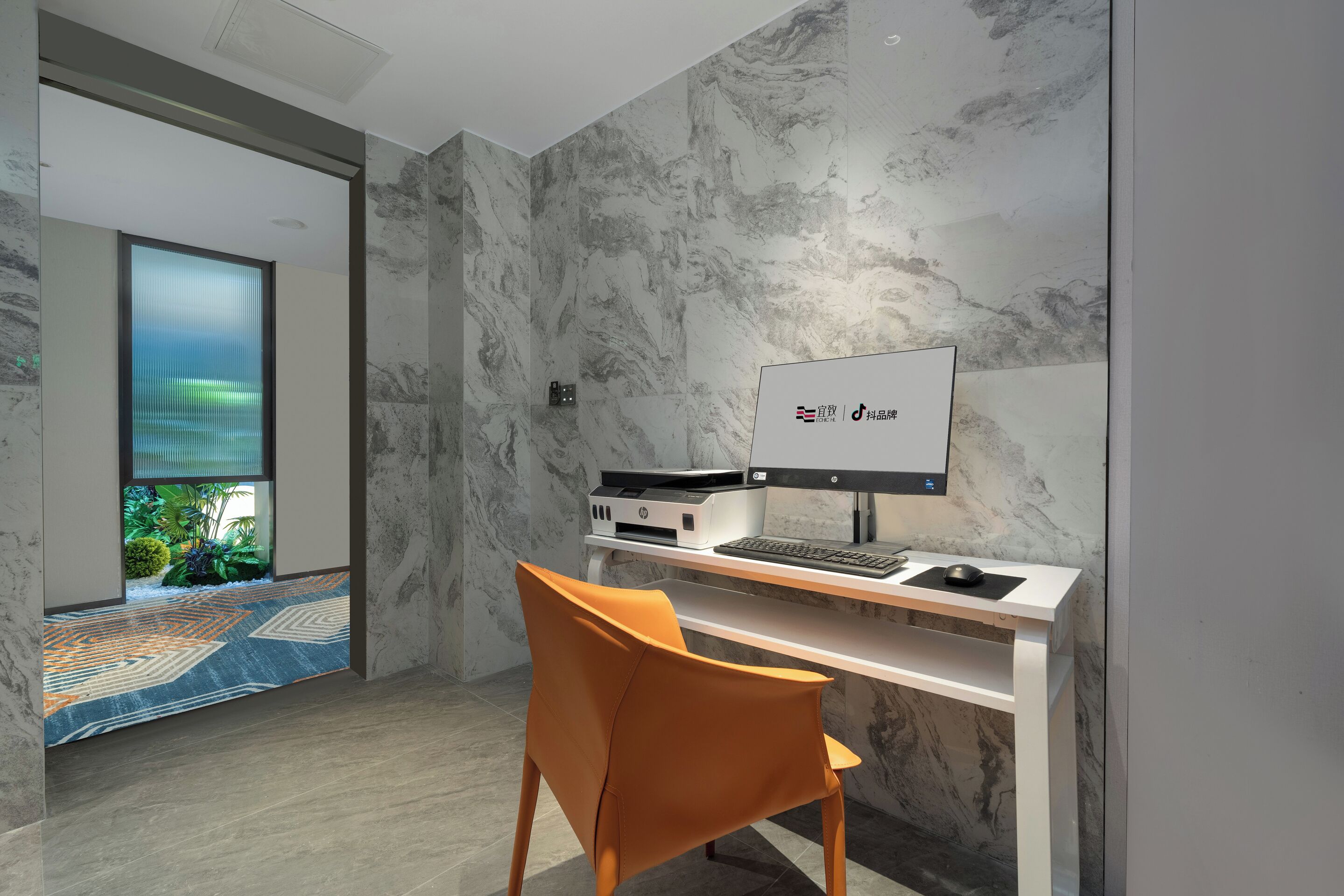 A modern office space with a desktop computer, a chair, and a view of a garden through a glass door.