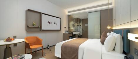 A modern hotel room with a bed, a desk, a chair, a small table with books, and a mirror.