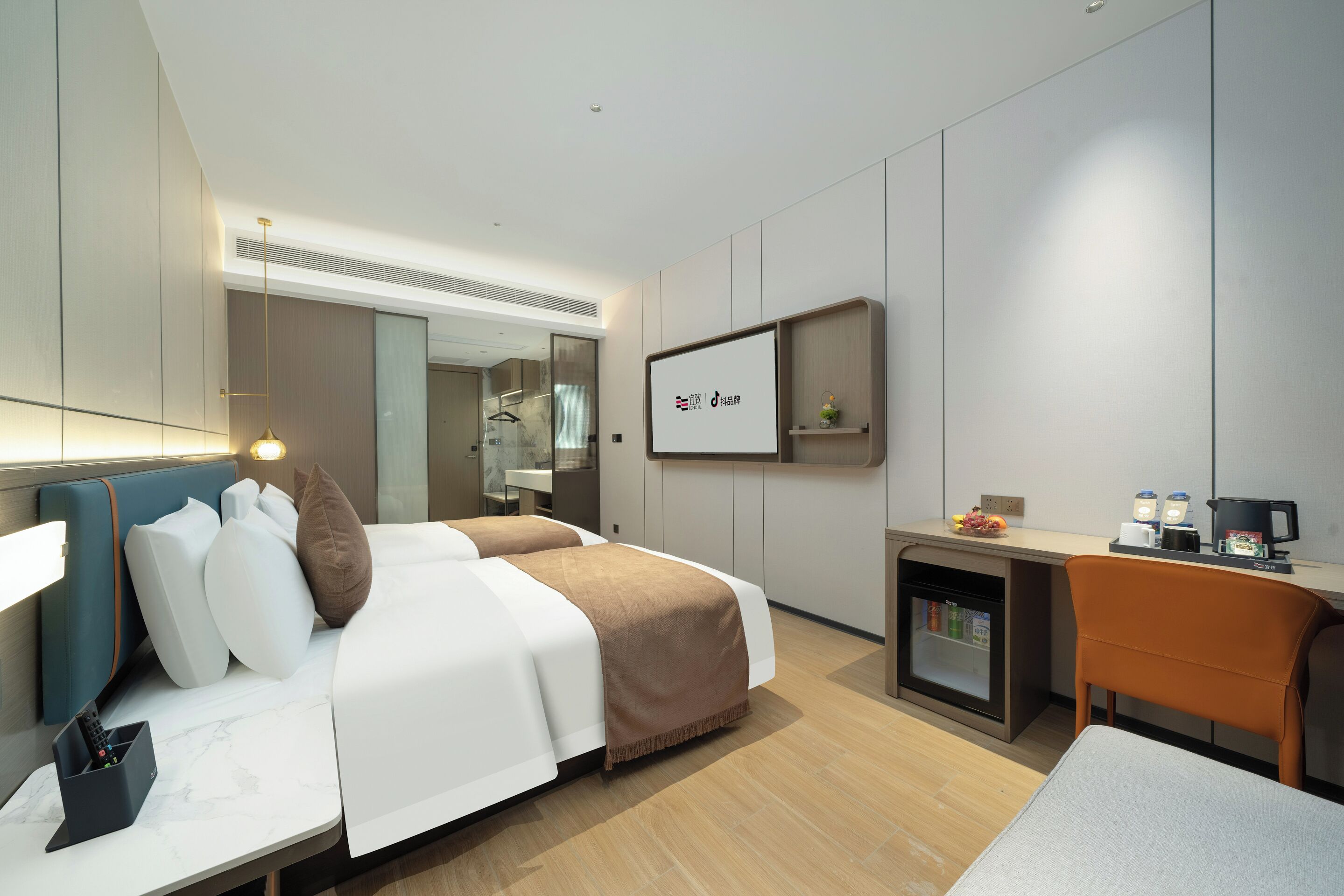 Una habitación de hotel moderna con cama, escritorio, silla, refrigerador y espejo.