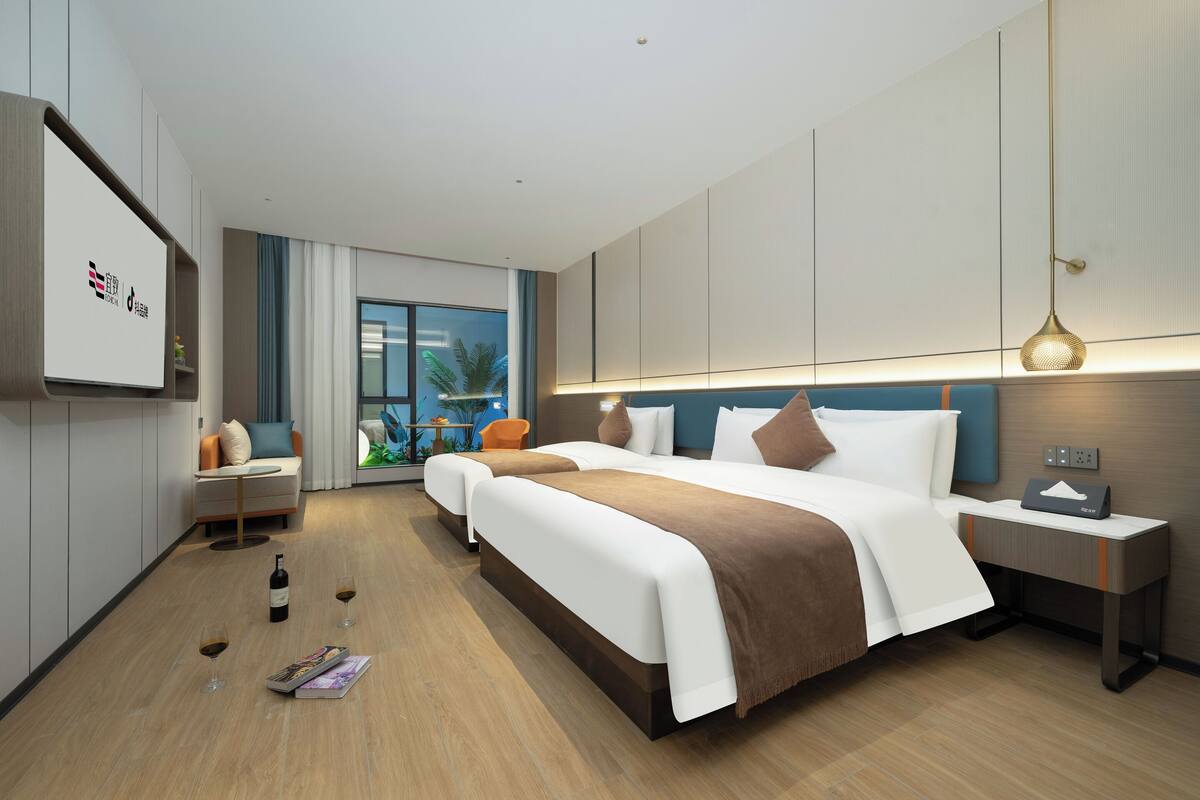 A modern hotel room with two beds, a sofa, a small table, and a nightstand.