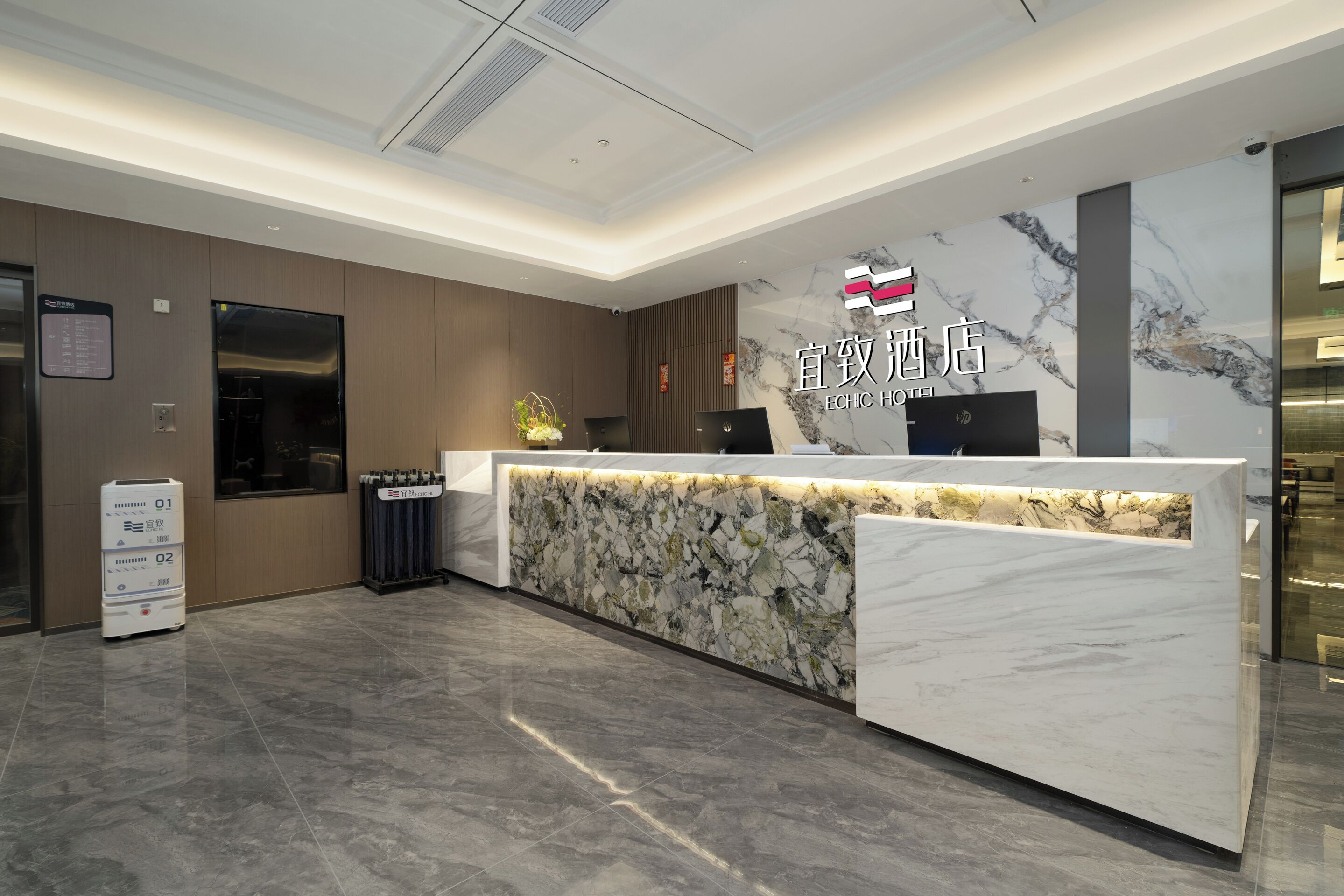 A hotel reception desk with a marble design, a digital screen, and a security camera.