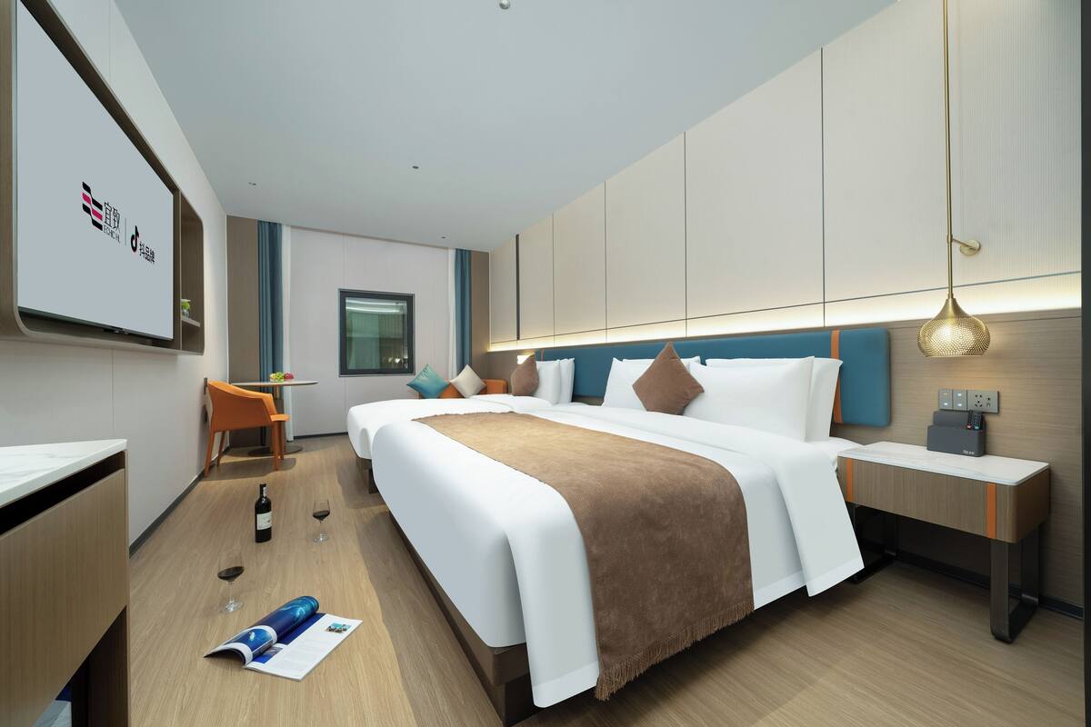 A modern hotel room with a large bed, bedside table, and a desk with a chair.