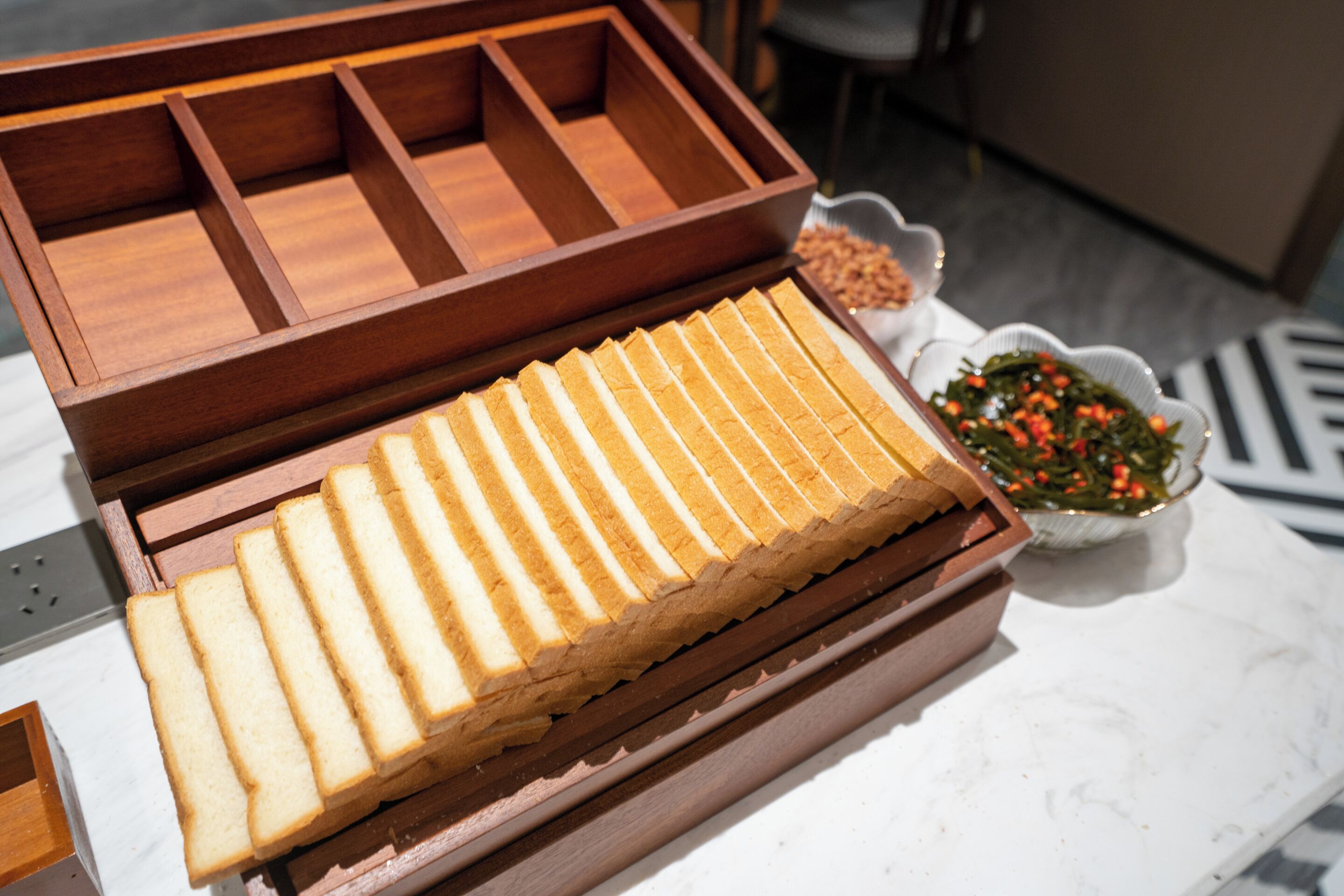A wooden box with compartments containing sliced bread and a small bowl of nuts.
