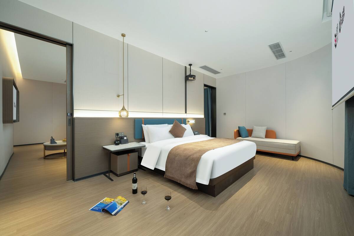 A modern hotel room with a large bed, bedside tables, a desk, and a seating area.