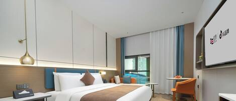A modern hotel room with a large bed, bedside table, and a desk with a chair. There is a window with curtains, a small table with a chair, and a TV mounted on the wall.
