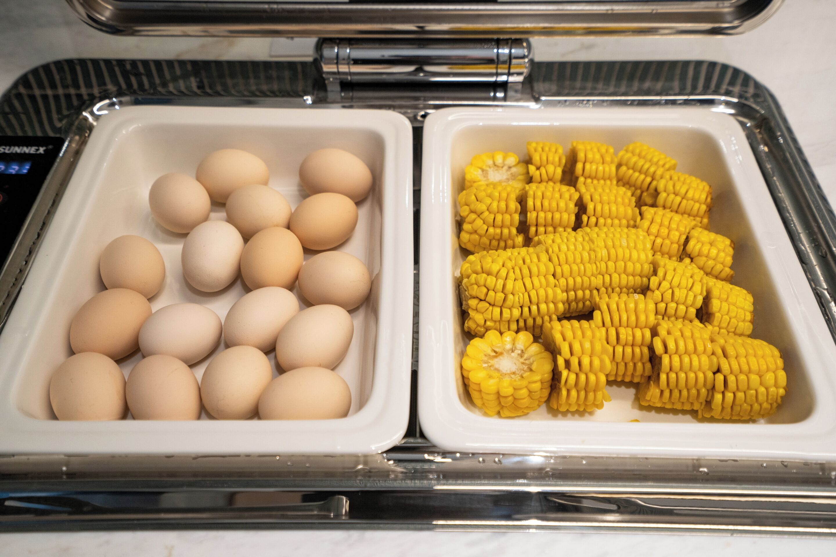 A food service area with two trays, one containing eggs and the other containing corn on the cob.