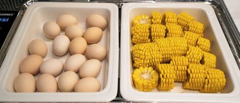 A food service area with two trays, one containing eggs and the other containing corn on the cob.
