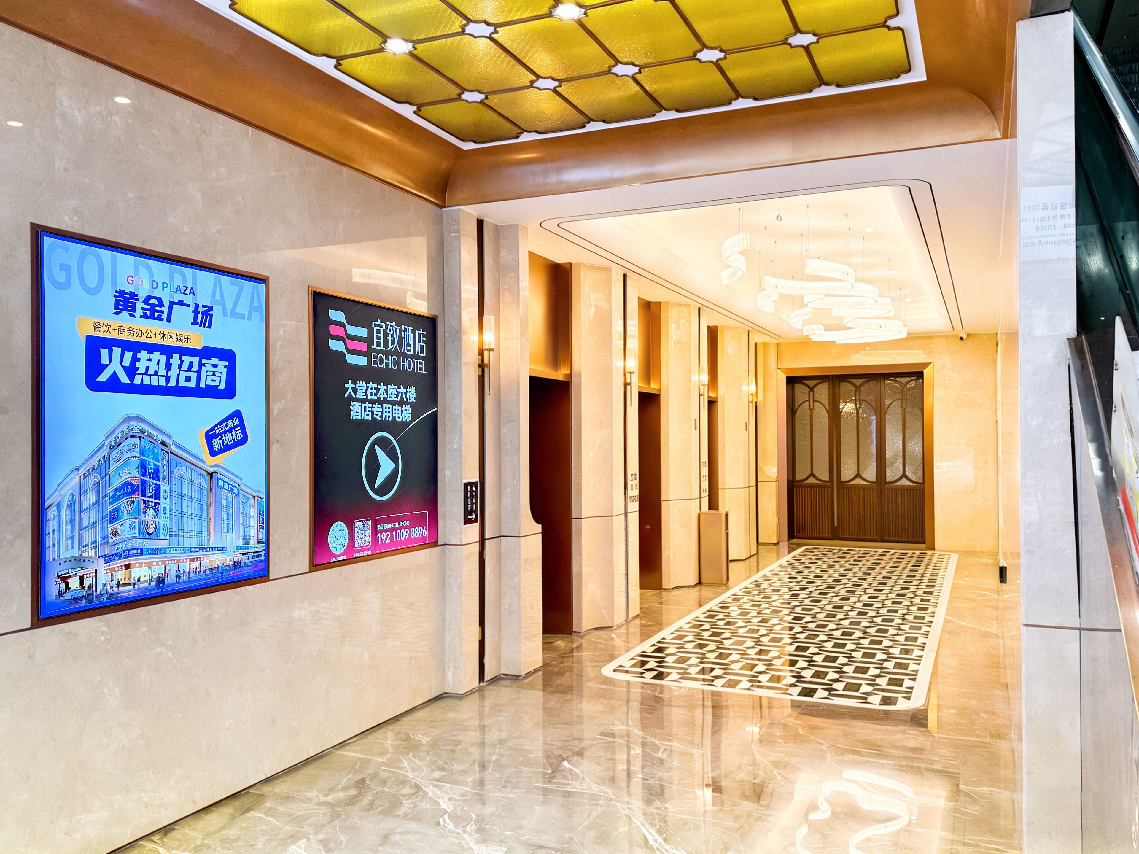 Un vestíbulo de hotel con diseño moderno, que incluye una pantalla digital, una alfombra estampada y una zona de recepción.