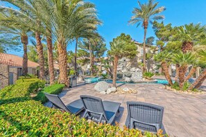 A poolside area with lounge chairs, palm trees, and a stone wall.