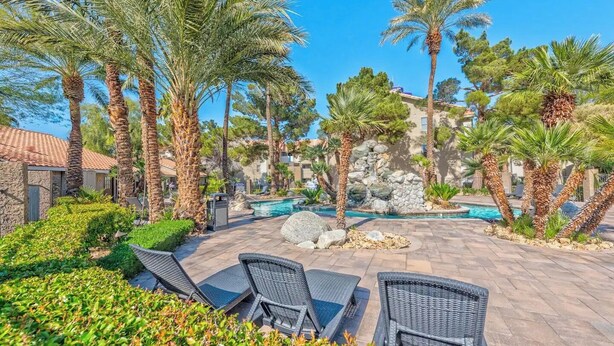 A poolside area with lounge chairs, palm trees, and a stone wall.