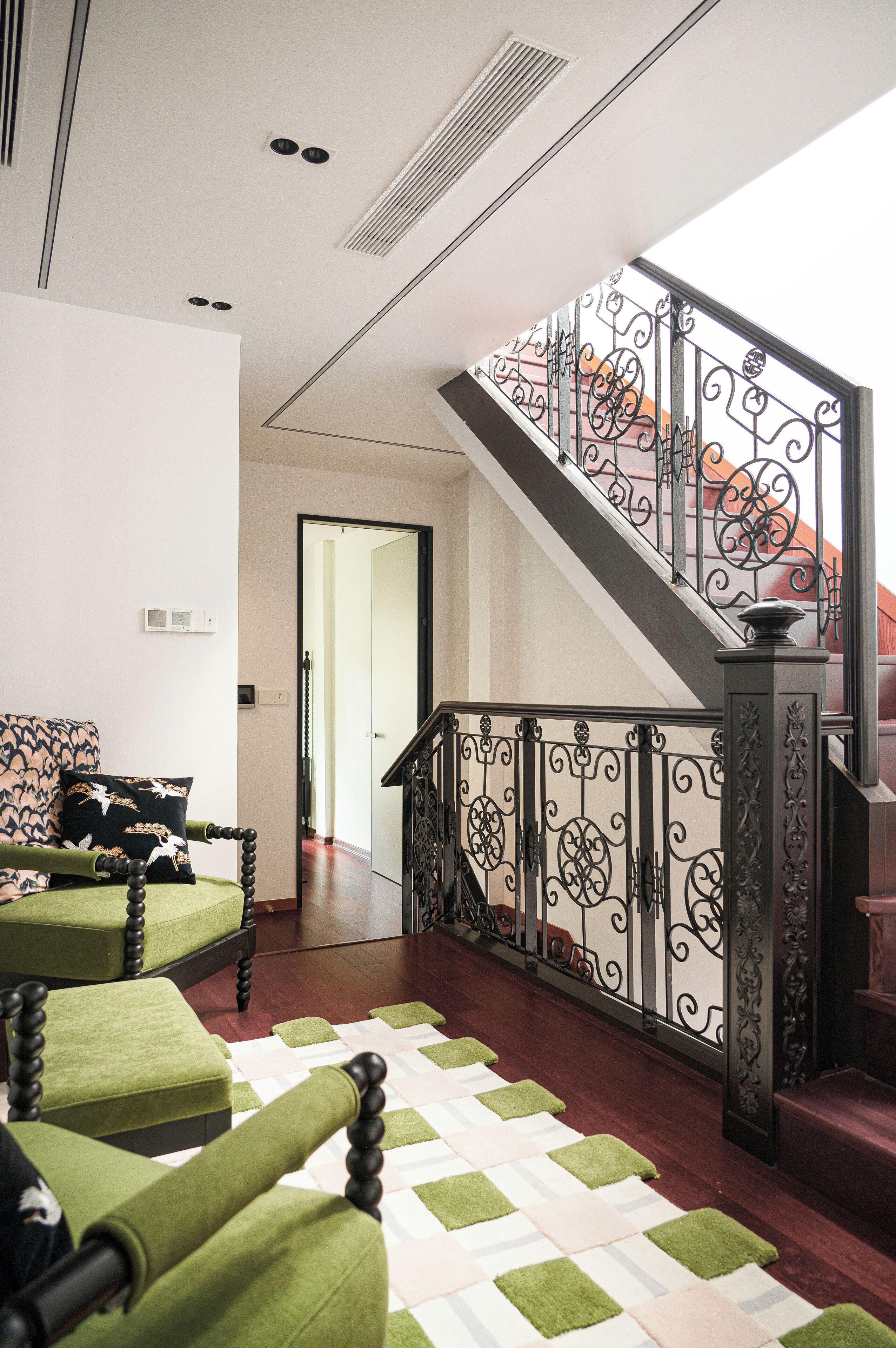 A staircase with ornate black railings, a checkered carpet, and a green upholstered sofa with a patterned cushion.