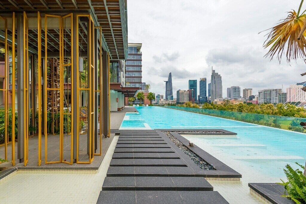 A rooftop pool with a city skyline view, a modern building with yellow accents, and a clear sky.