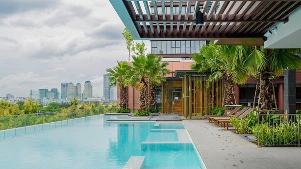 A rooftop swimming pool with a city skyline view, palm trees, and lounge chairs.