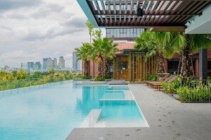 A rooftop swimming pool with a city skyline view, palm trees, and lounge chairs. - Gallery Residence - Metropole Thu Thiem (Ho Chi Minh City)