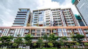A multi-story building with a modern architectural design, featuring a mix of glass and metal facade, and a landscaped front area with trees.
