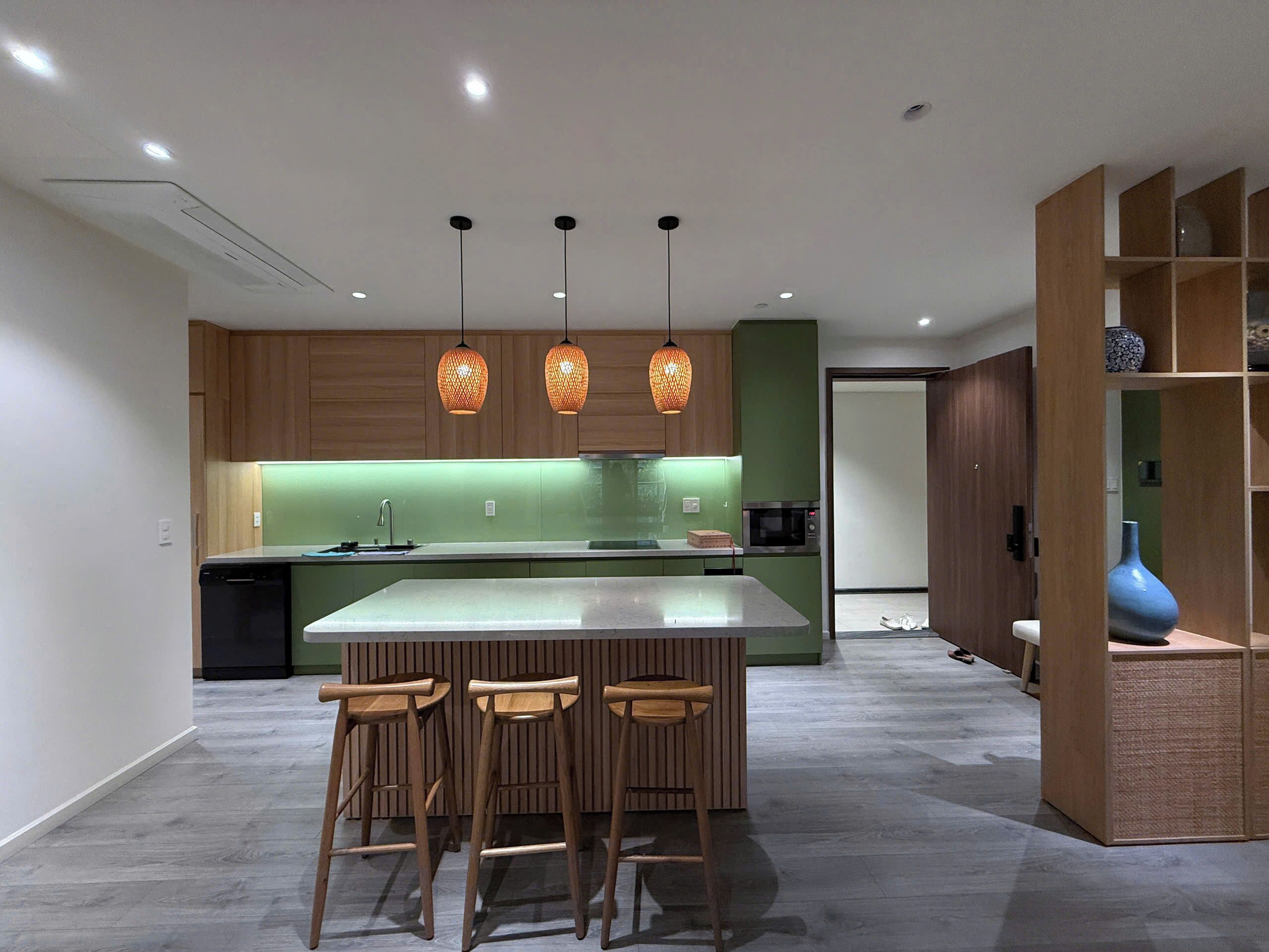 A modern kitchen with a central island, wooden bar stools, pendant lighting, and a built-in microwave.
