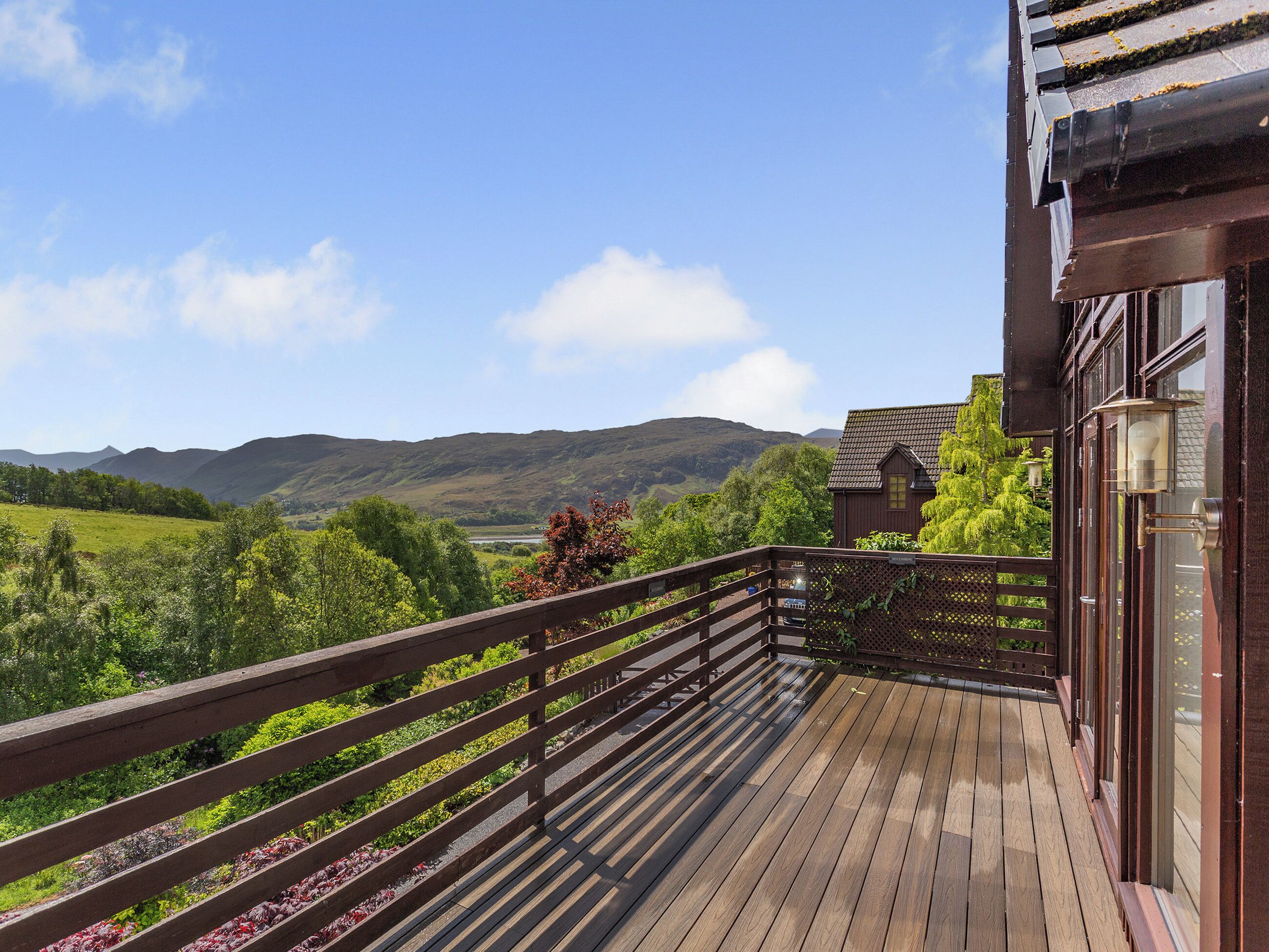 Eine Holzterrasse mit Blick auf grüne Hügel und ein Haus im Hintergrund.