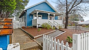 Une maison bleue avec un porche, une clôture en bois peinte en blanc et un petit jardin.