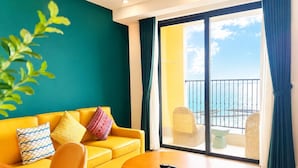 A yellow sofa with patterned cushions, a round wooden table, and a view of the sea through a balcony with wicker chairs. - Aura Apartment (Phu Quoc)