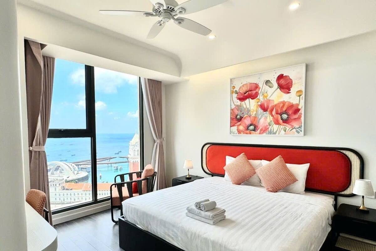 A hotel room with a large bed, a view of the sea, and a ceiling fan.