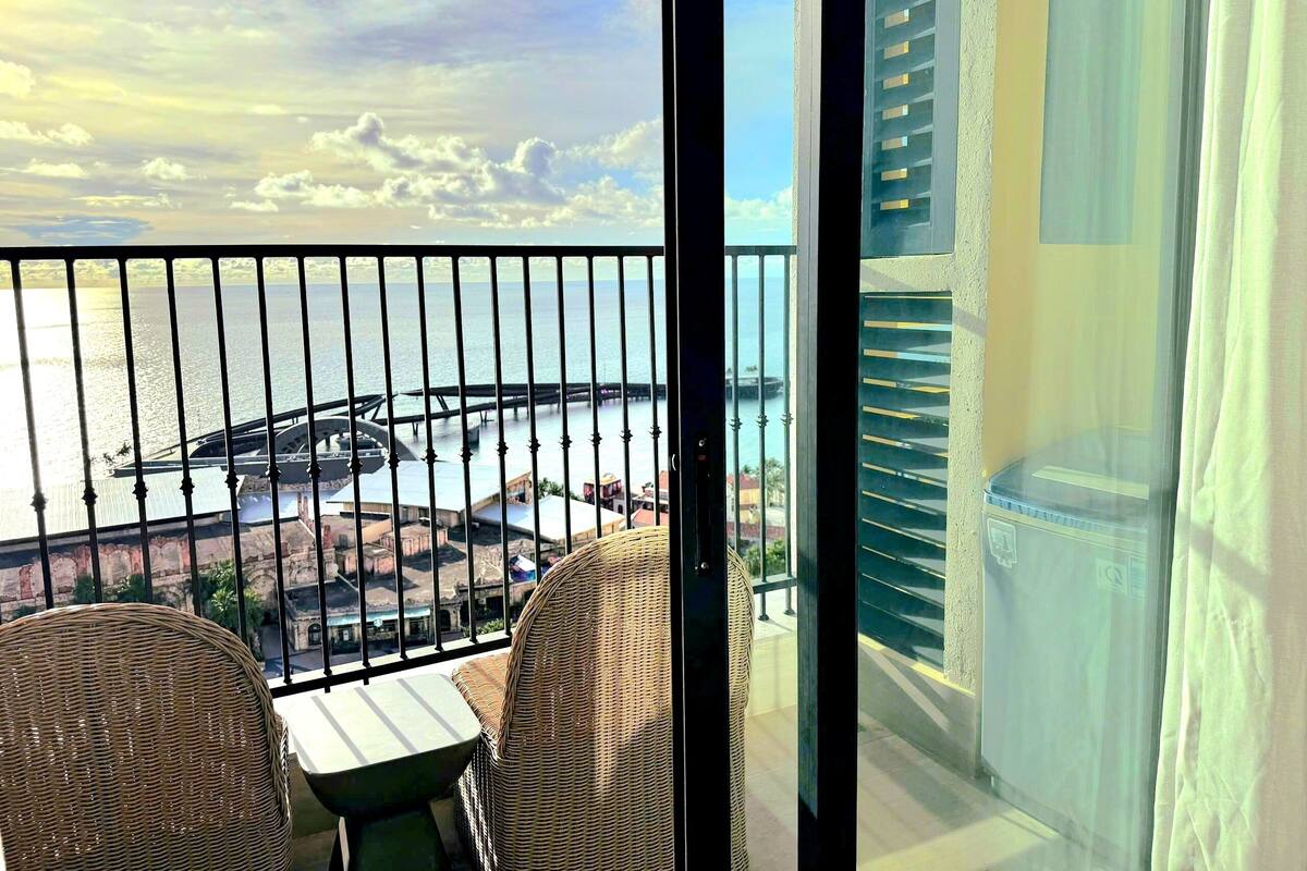 A balcony with wicker furniture, a view of a bridge, and a body of water.