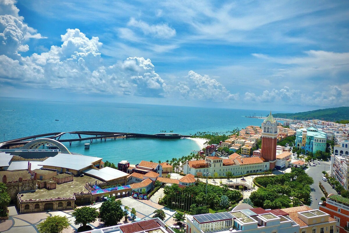 A coastal cityscape with a prominent clock tower, a bridge, and a marina.