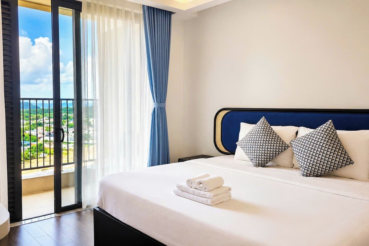 A hotel room with a bed, a view through a sliding door, and a balcony.