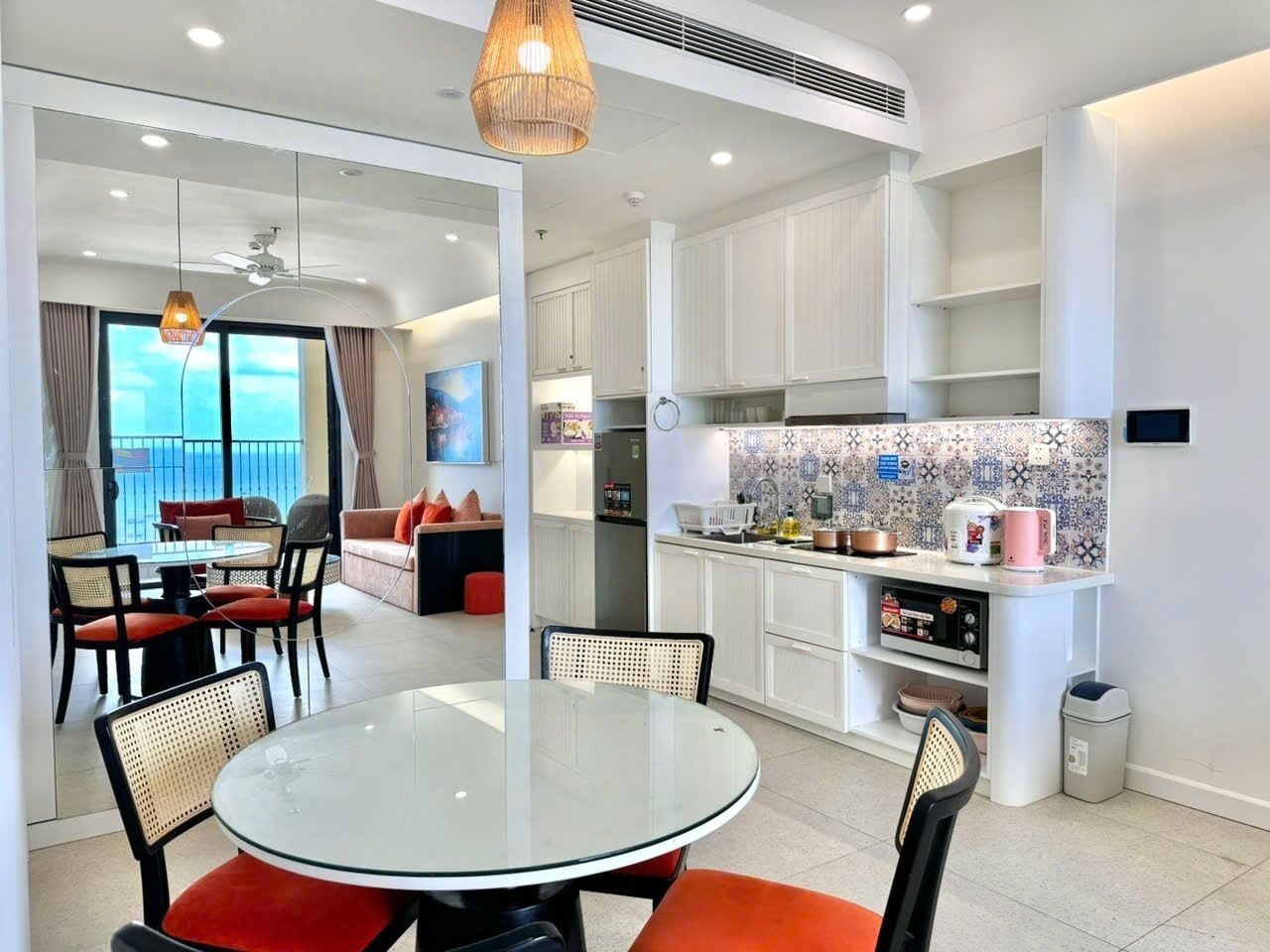 A modern kitchen with white cabinets, a dining area with a glass table, and a balcony with outdoor seating.