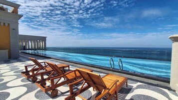 Una piscina infinita en la azotea con sillones de madera y suelo estampado.