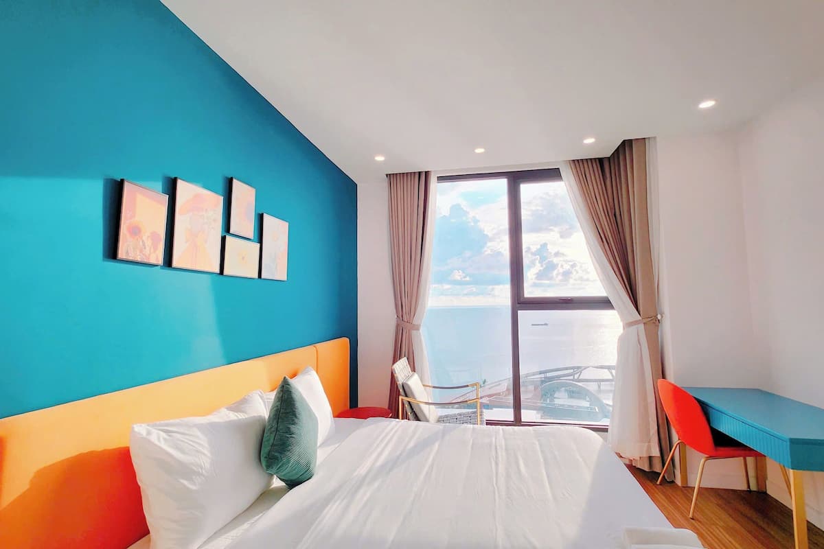 A hotel room with a bed, a desk, and a view of the sea.
