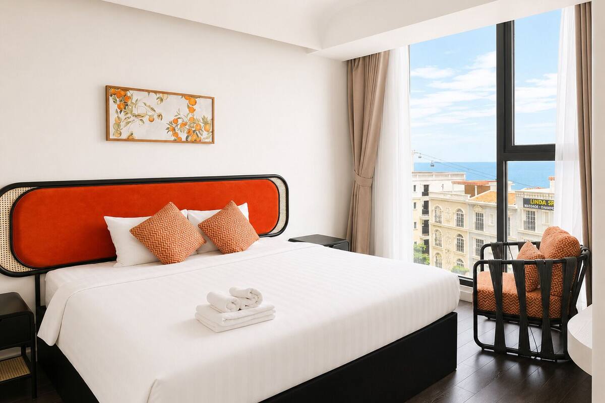 A hotel room with a large bed, a view of the city, and a chair by the window.