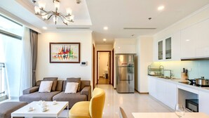 A modern living room with a sofa, a yellow armchair, and a coffee table. There is a kitchen area with white cabinets and a refrigerator.