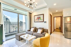 A modern living room with a sofa, ottoman, and coffee table, a large window with a city view, and a painting on the wall. - Landmark Plus . Vinhomes Central Park (Ho Chi Minh City)