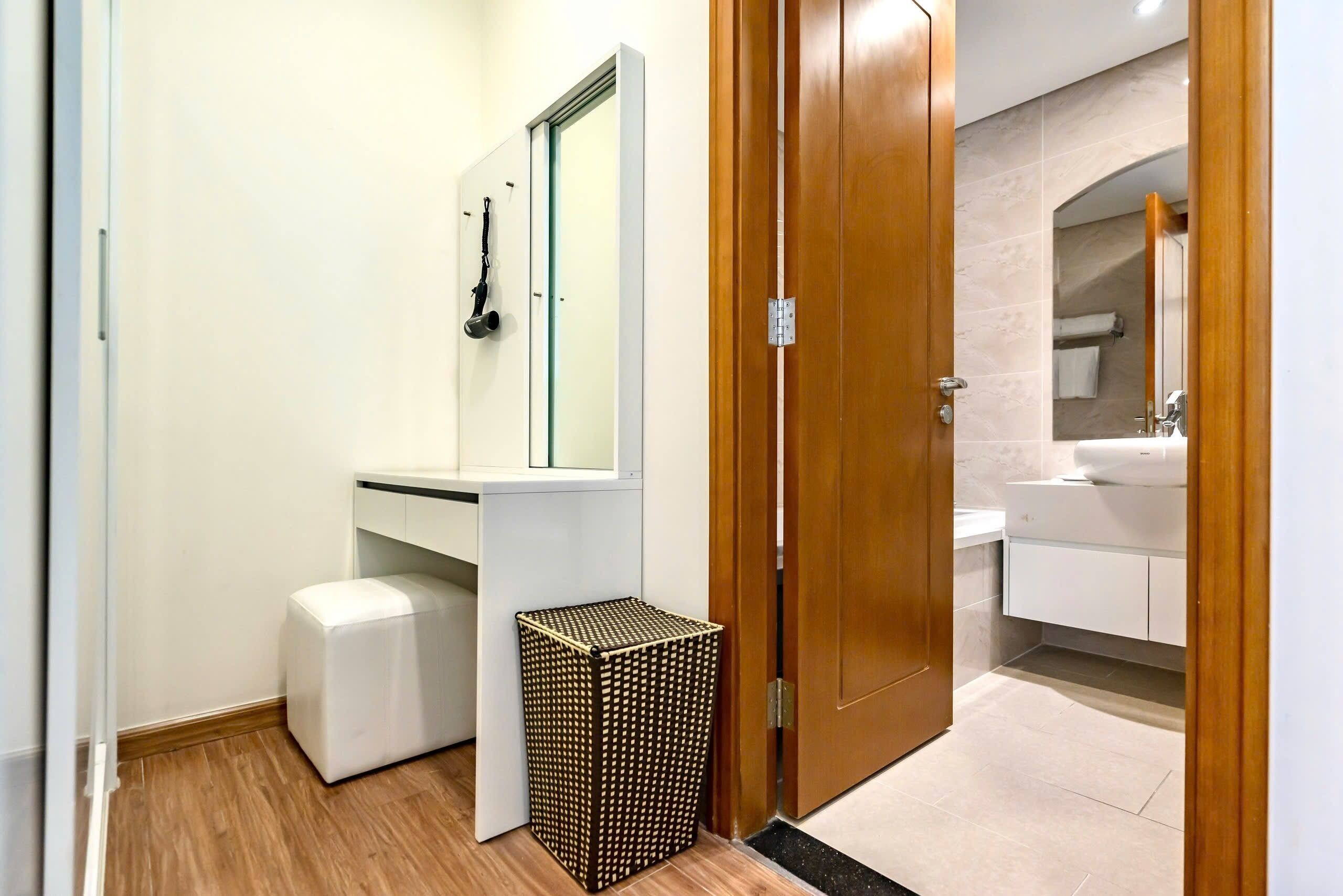 A bathroom with a white vanity, a mirror, a white toilet, and a small trash bin.