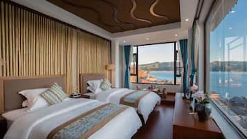 A hotel room with two beds, a large window with a view of a body of water and hills, and a bamboo wall.