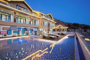 A modern hotel with a large outdoor swimming pool, lounge chairs, and a colorful wall design. - Lugu Lake Yunshang Holiday Hotel (Liangshan Yi)