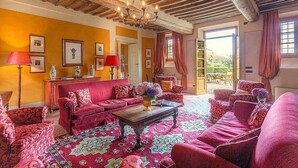 A room with a wooden ceiling, red upholstered furniture, a patterned rug, and framed pictures on the walls.
