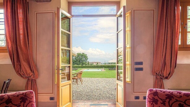 An open doorway leading to a courtyard with a lawn, gravel path, and outdoor furniture.