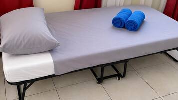 Una cama individual con colchón gris, almohada blanca y dos toallas enrolladas en azul.