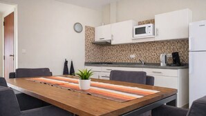 Une cuisine moderne avec des meubles blancs, un four à micro-ondes et une machine à café. On y trouve une table à manger avec des chaises et une plante.