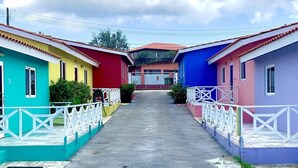 Une rangée de maisons colorées avec des balustrades blanches, un chemin pavé et, au loin, un bâtiment doté d’un toit rouge.