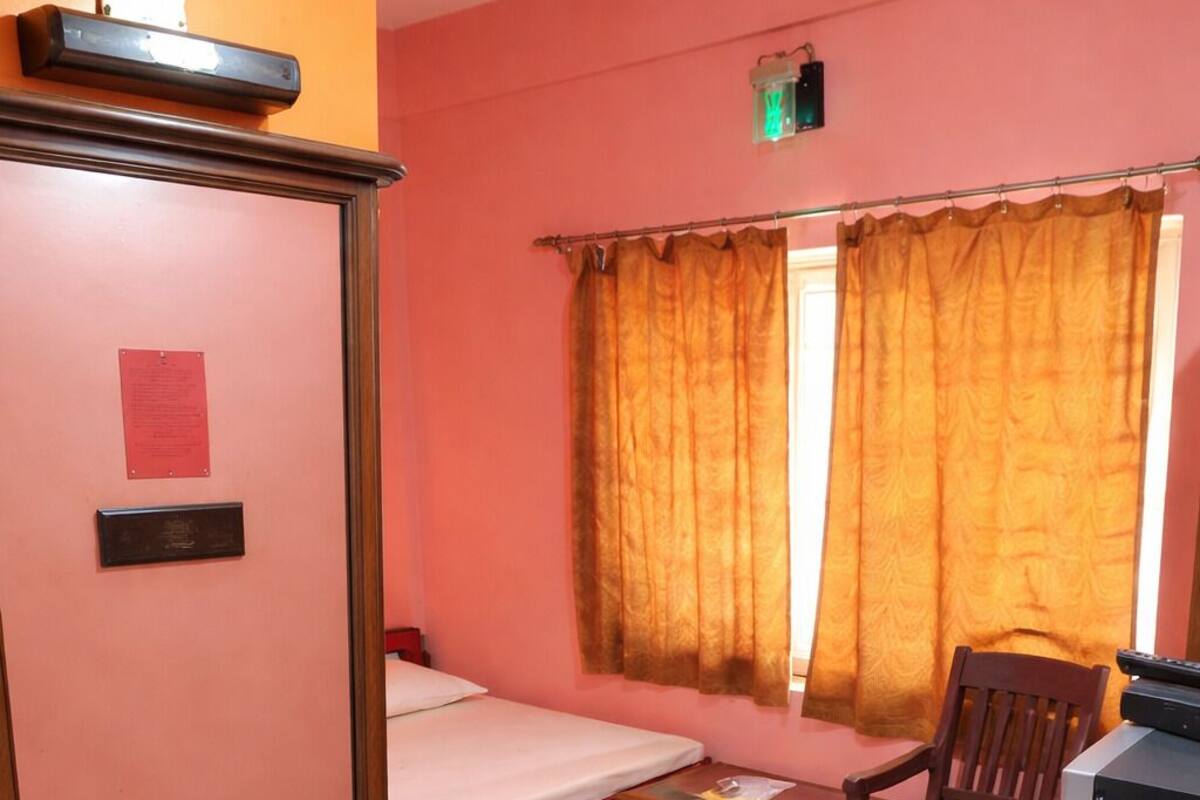 Une pièce comprenant un lit, un bureau en bois, une chaise, un téléviseur et une fenêtre avec des rideaux.