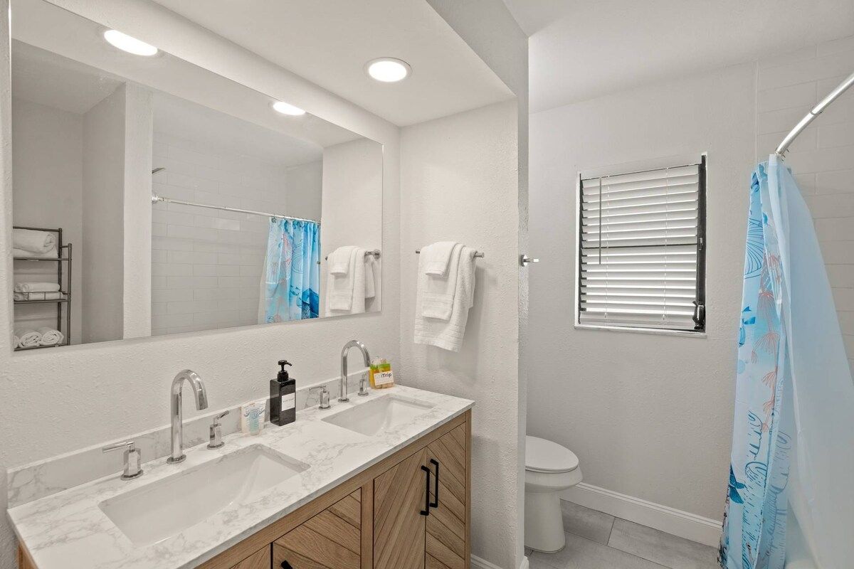 A bathroom with a double sink, a large mirror, a shower with a curtain, and a toilet.