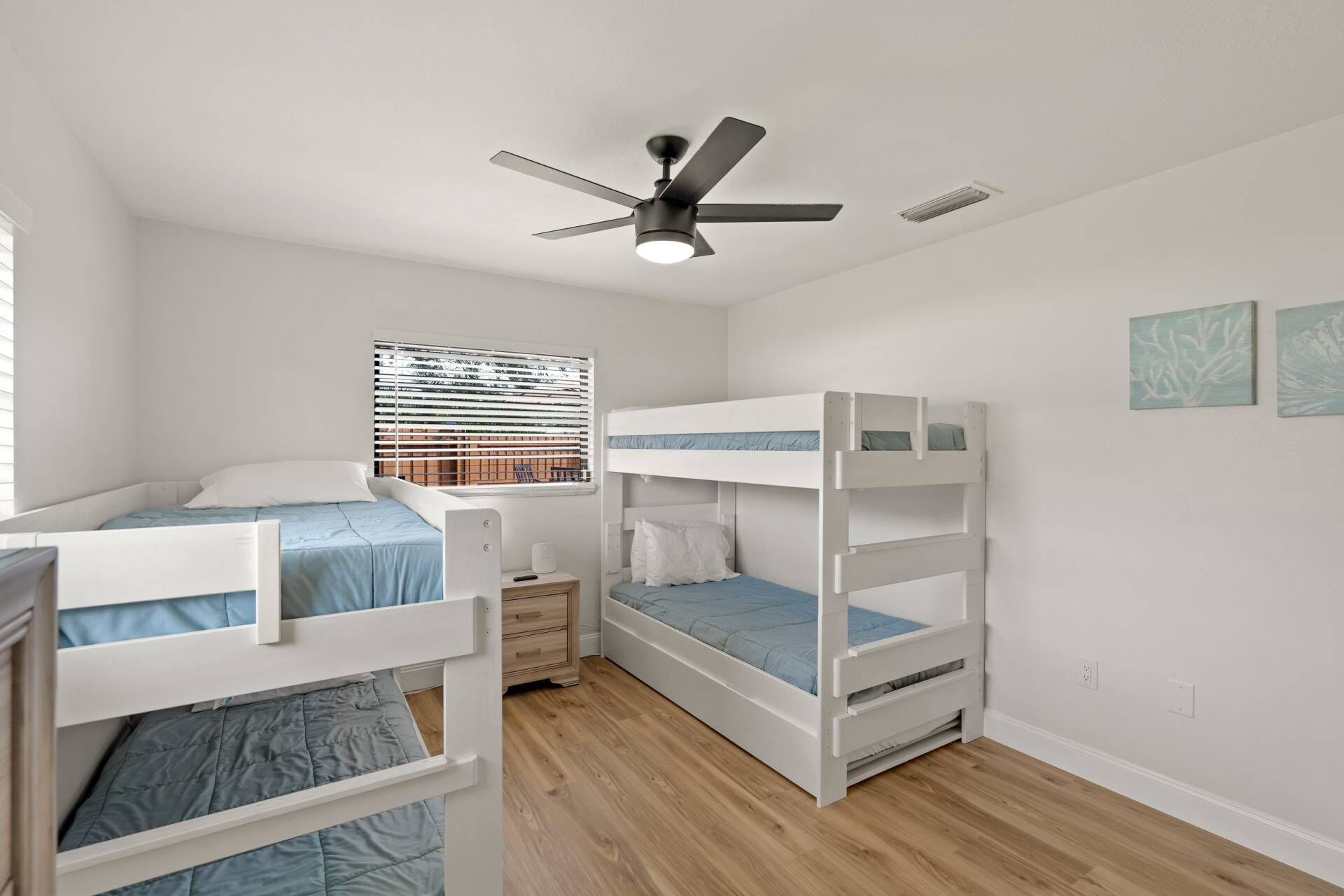 Ein Schlafzimmer mit Etagenbetten, Deckenventilator, Fenster mit Jalousien und zwei Wandbildern.