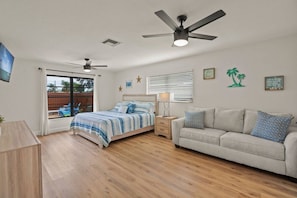 Ein Schlafzimmer mit einem Bett, einem Schlafsofa, einem Deckenventilator, einem Fenster und Blick ins Freie.
