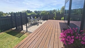 Terraza de madera con mesa y sillas, rodeada por una valla y plantas en macetas.