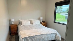 Un dormitorio con una cama grande, dos mesitas de noche, un ventanal con vistas al verdor y una lámpara en el techo.