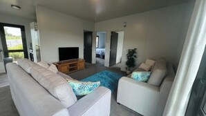Una sala de estar moderna con un conjunto de sofá, una mesa de centro y un televisor. Hay puertas que dan a otras habitaciones.