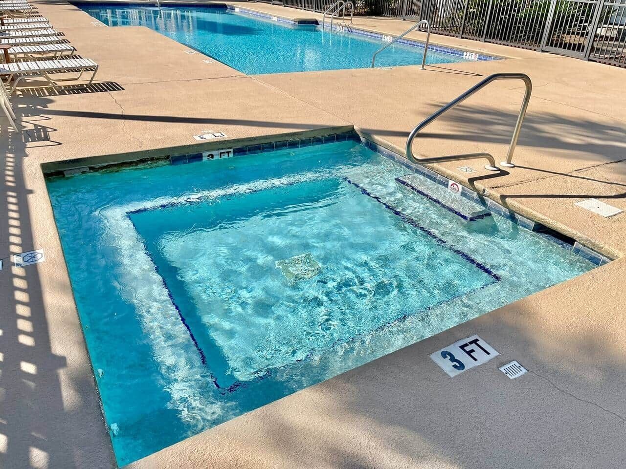 A swimming pool with a 3 FT depth marker, poolside lounge chairs, and a metal ladder.